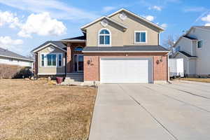 Split level home with concrete driveway, brick siding, an attached garage, and stucco siding