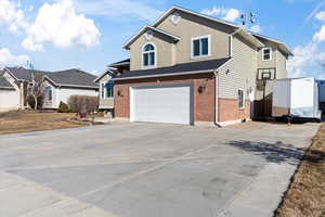 View of front facade featuring a garage, brick siding, driveway, and stucco siding