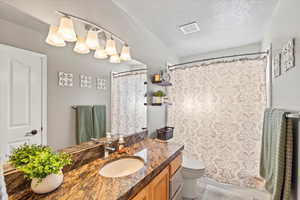 Full bath featuring curtained shower, visible vents, toilet, a textured ceiling, and vanity