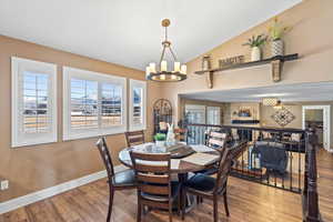 Dining area featuring a chandelier, vaulted ceiling, baseboards, and wood finished floors