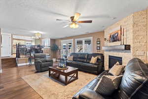 Living area featuring baseboards, dark wood-type flooring, a textured ceiling, a fireplace, and ceiling fan with notable chandelier