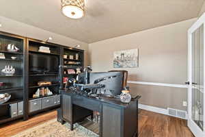 Office space with baseboards, a textured ceiling, visible vents, and wood finished floors