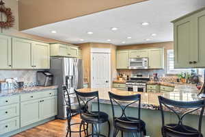 Kitchen featuring stainless steel appliances, green cabinets, light wood-style floors, a sink, and a peninsula