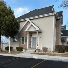 View of front facade with uncovered parking, brick siding, a shingled roof, and stucco siding