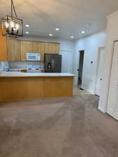Kitchen featuring white appliances, light colored carpet, hanging light fixtures, a textured ceiling, and recessed lighting