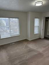 Empty room with a textured ceiling, carpet, visible vents, and baseboards