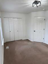 Unfurnished bedroom featuring dark colored carpet, a closet, visible vents, a textured ceiling, and baseboards