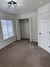Unfurnished bedroom with visible vents, baseboards, a textured ceiling, carpet flooring, and a closet