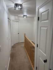 Corridor with carpet floors, baseboards, a textured ceiling, and an upstairs landing