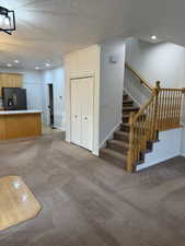 Unfurnished living room with light carpet, baseboards, stairway, a textured ceiling, and recessed lighting