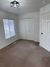 Unfurnished bedroom with a closet, a textured ceiling, visible vents, and carpet flooring