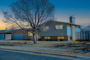 Split level home featuring driveway, a chimney, an attached garage, fence, and brick siding