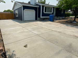 View of front facade with a garage, concrete driveway, a chimney, fence, and board and batten siding