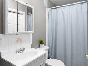 Bathroom featuring tasteful backsplash, a shower with shower curtain, vanity, and toilet