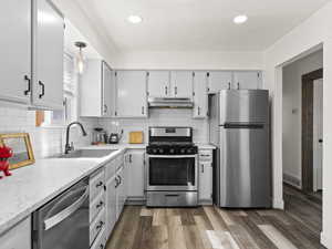 Kitchen with under cabinet range hood, a sink, visible vents, appliances with stainless steel finishes, and dark wood-style floors