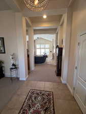 Hallway featuring lofted ceiling, light carpet, light tile patterned flooring, a chandelier, and baseboards