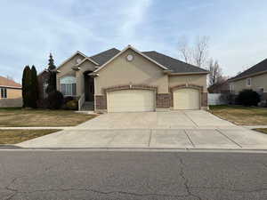 View of front facade featuring brick siding, stucco siding, an attached garage, driveway, and a front lawn