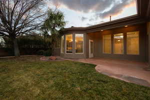 Back of house at dusk featuring a patio, a lawn, and stucco siding