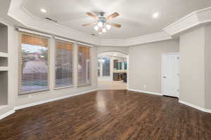 Unfurnished room with ceiling fan, arched walkways, wood finished floors, visible vents, and baseboards