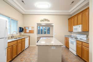 Club House. Kitchen with a tray ceiling, visible vents, a kitchen island, a sink, and white appliances