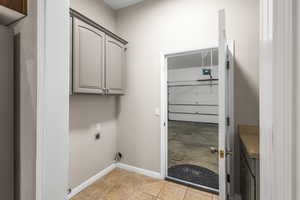 Laundry area with cabinet space, baseboards, hookup for an electric dryer, and light tile patterned flooring