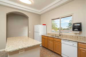 Club House. Kitchen featuring white appliances, arched walkways, light stone counters, brown cabinets, and a sink