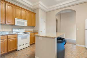 Club House. Kitchen with arched walkways, white appliances, light tile patterned floors, and light stone countertops