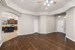 Unfurnished living room with light wood-style flooring, arched walkways, ceiling fan, and baseboards