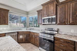 Kitchen with light stone counters, stainless steel appliances, light tile patterned flooring, a sink, and dark brown cabinets