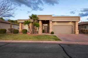 View of front of house featuring a garage, concrete driveway, stone siding, a front lawn, and stucco siding