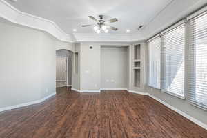 Interior space featuring arched walkways, ceiling fan, wood finished floors, visible vents, and baseboards