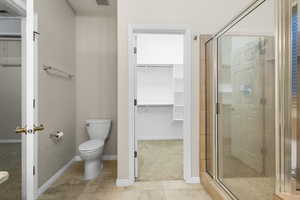 Full bath featuring toilet, tile patterned flooring, a shower stall, and a walk in closet