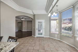 Unfurnished dining area featuring light tile patterned floors, baseboards, arched walkways, a tray ceiling, and ceiling fan with notable chandelier