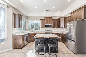 Kitchen with light tile patterned floors, appliances with stainless steel finishes, a raised ceiling, and a center island