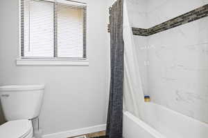 Full bath featuring toilet, baseboards, and shower / bath combo with shower curtain