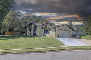 View of front of property featuring driveway, a garage, a lawn, fence, and brick siding