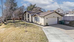 View of front of house with brick siding, an attached garage, board and batten siding, a front yard, and driveway