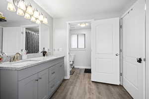 Full bath with double vanity, wood finished floors, a sink, and toilet