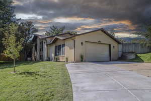 View of front of home featuring concrete driveway, fence, a lawn, and brick siding