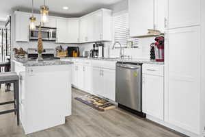 Kitchen featuring light wood finished floors, appliances with stainless steel finishes, white cabinets, a sink, and light stone countertops