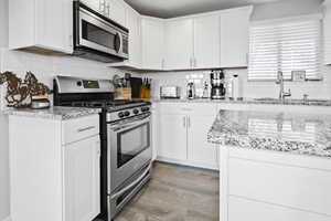 Kitchen with stainless steel appliances, backsplash, light wood-style flooring, white cabinetry, and a sink