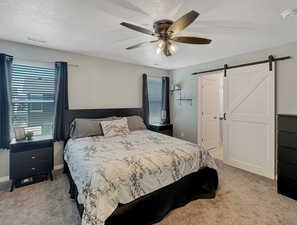 Bedroom featuring a textured ceiling, visible vents, ceiling fan, a barn door, and light carpet