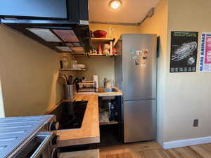 Kitchen with open shelves, light countertops, freestanding refrigerator, a sink, and black electric cooktop