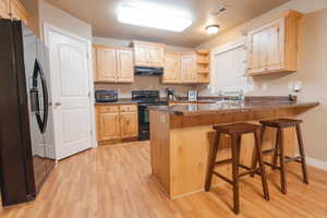 Kitchen with light wood finished floors, light brown cabinets, a peninsula, under cabinet range hood, and black appliances