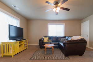 Carpeted living area featuring visible vents, ceiling fan, and baseboards