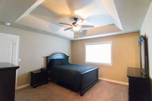 Bedroom with light carpet, ceiling fan, baseboards, and a raised ceiling