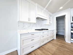 Kitchen featuring appliances with stainless steel finishes, light countertops, light wood-type flooring, white cabinetry, and backsplash