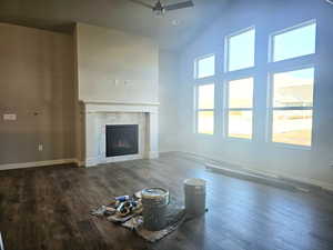 Unfurnished living room with a fireplace, a ceiling fan, wood finished floors, high vaulted ceiling, and baseboards