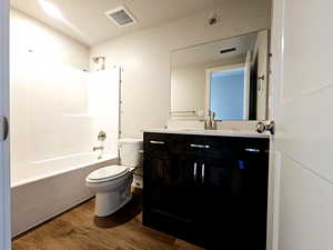 Bathroom with shower / bathtub combination, toilet, wood finished floors, vanity, and visible vents