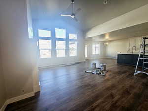 Unfurnished living room with high vaulted ceiling, dark wood-style floors, baseboards, and a ceiling fan